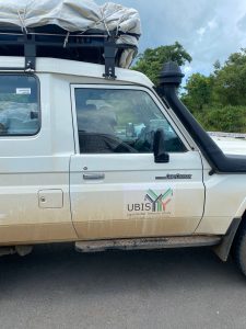 A picture of a white Toyota Landcruiser, somewhat dirty and loaded on the roof. A decal on the side reads UBIS, Uganda Bat Immune Study. Muni and Bucknell University